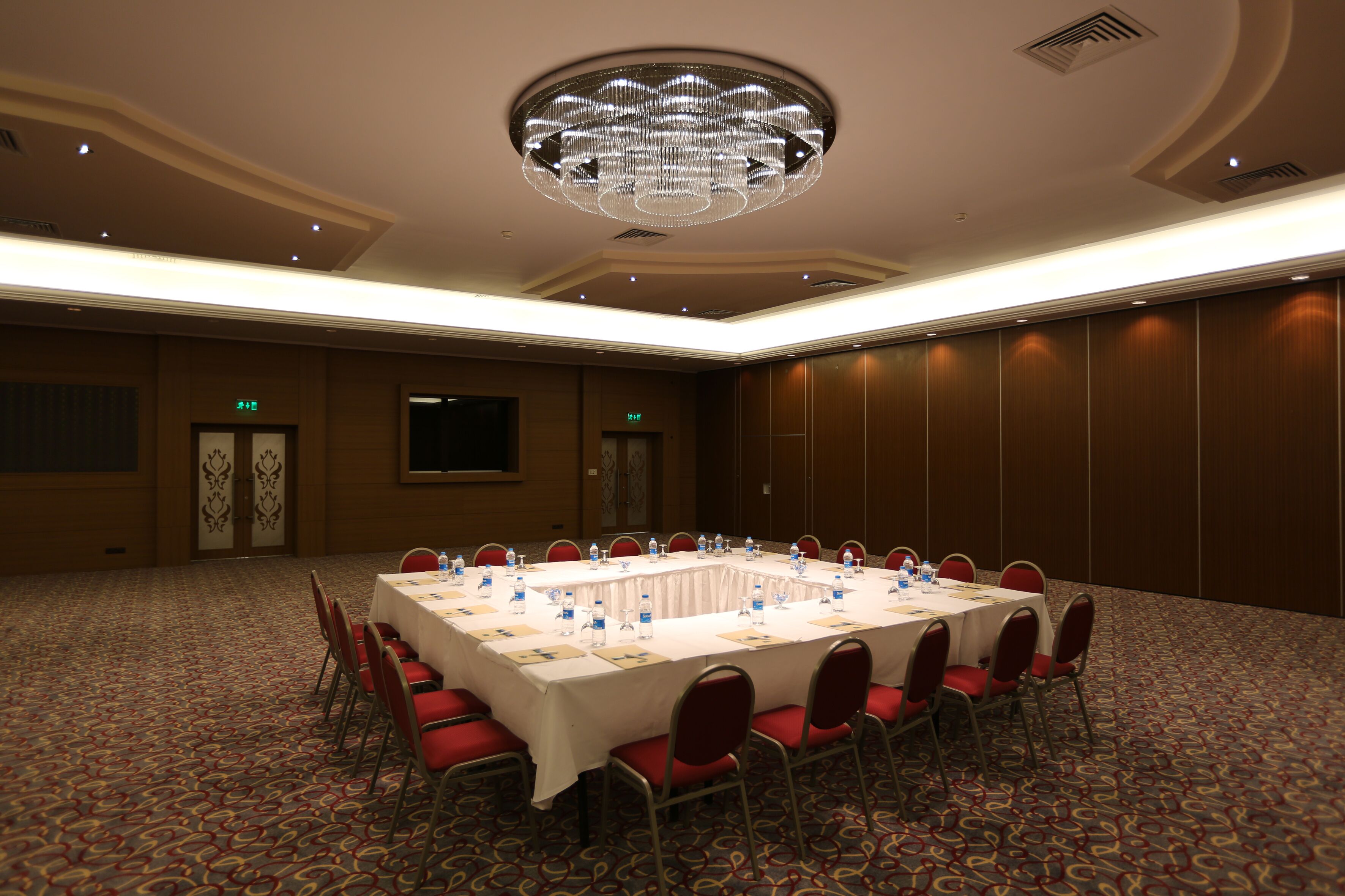 Une salle de conférence avec une longue table, des chaises rouges et un lustre.