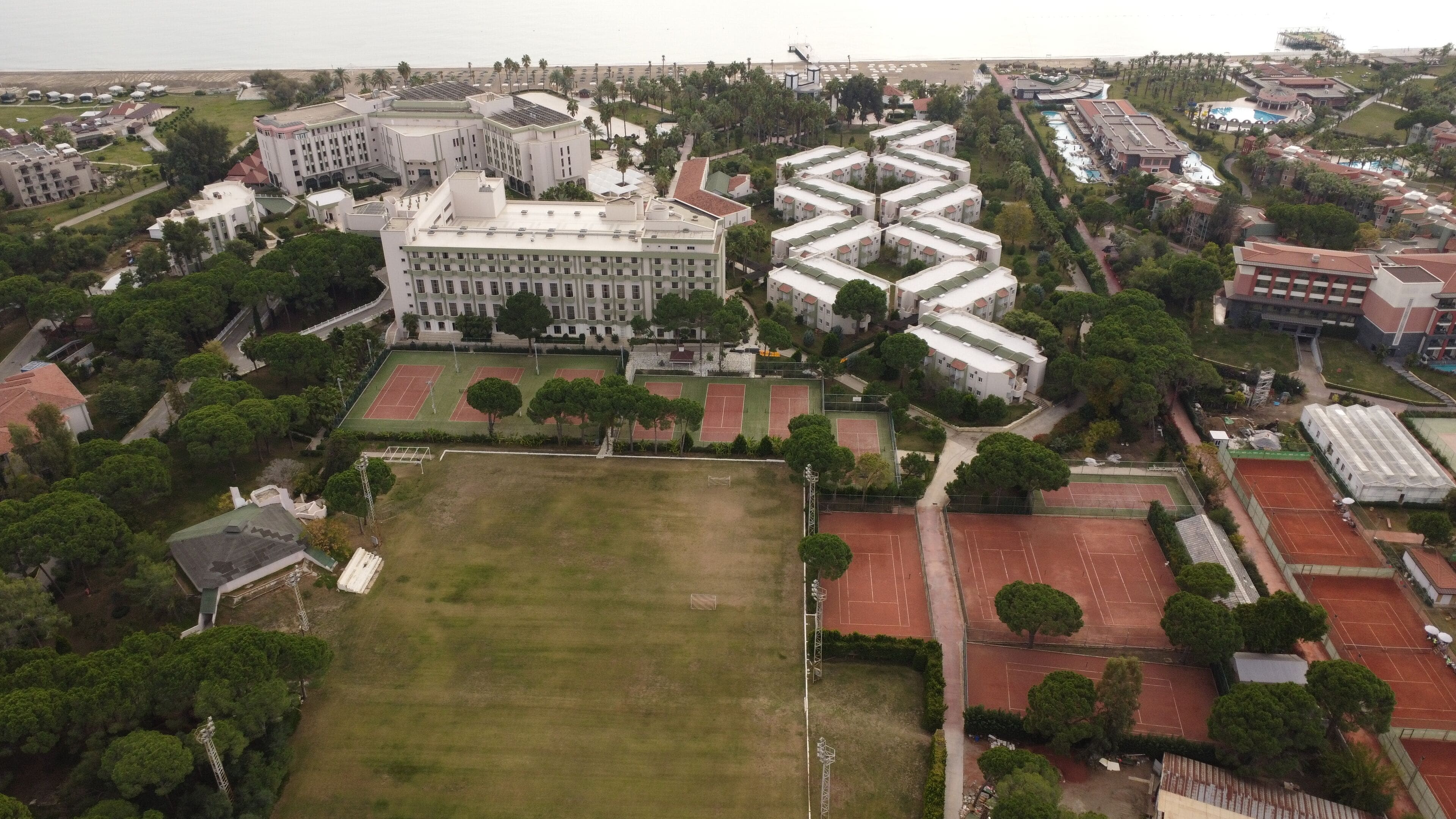 An aerial view of a large hotel complex with multiple buildings, tennis courts, and surrounding greenery.