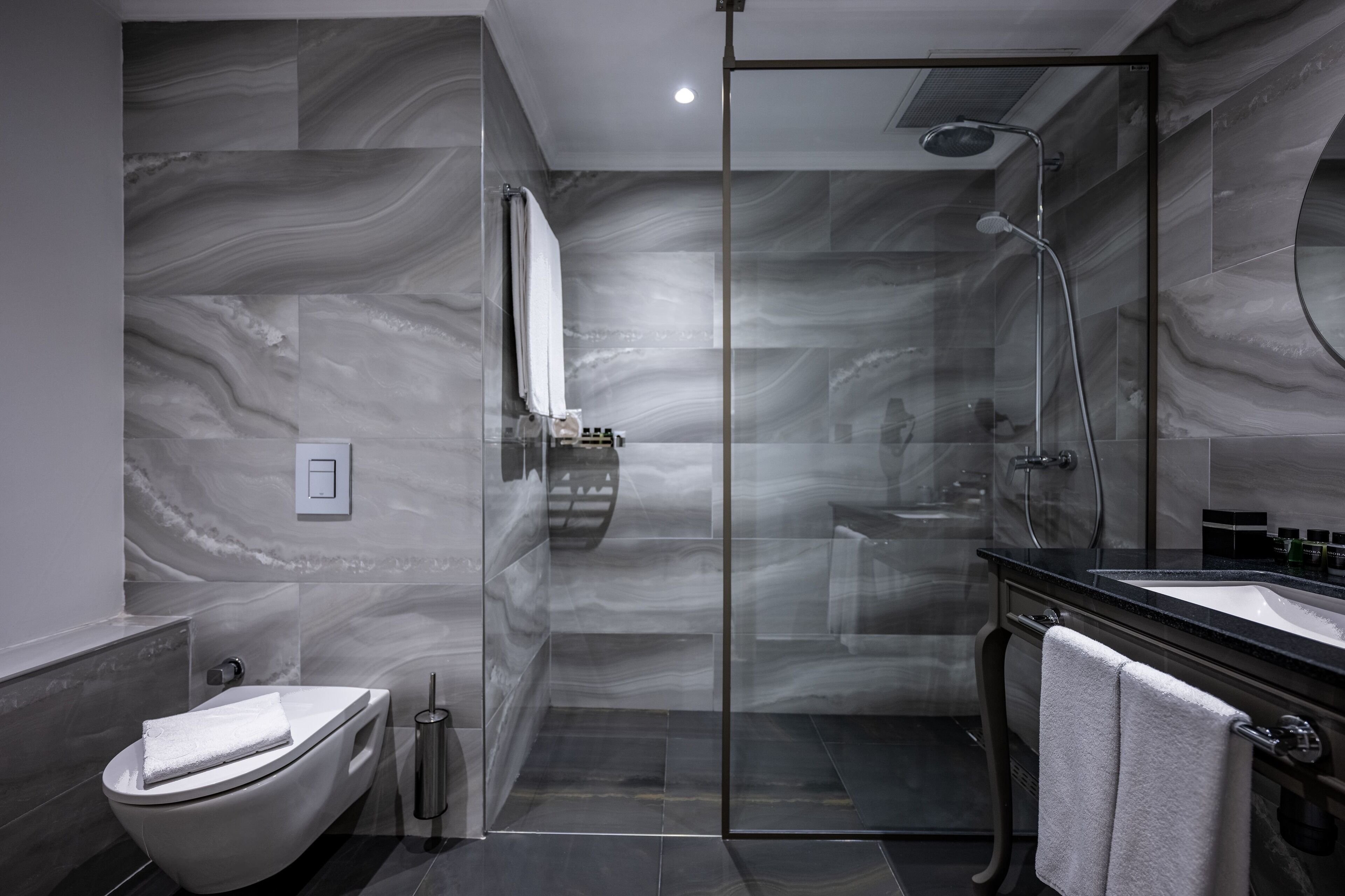 Un baño moderno con ducha envuelta en vidrio, inodoro blanco y lavamanos negro con espejo.