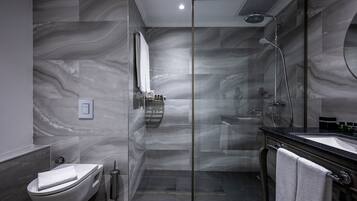 Un baño moderno con ducha envuelta en vidrio, inodoro blanco y lavamanos negro con espejo.