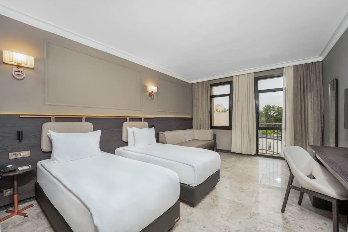 Ein Hotelzimmer mit zwei Betten, einem Schlafsofa, einem Schreibtisch und einem Sessel.