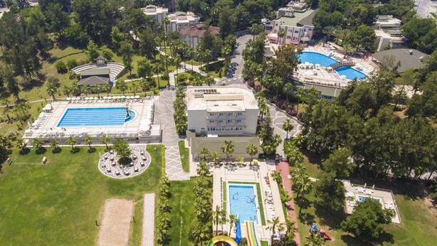 Vue aérienne d’un complexe hôtelier doté de plusieurs piscines, d’un bâtiment central et d’un espace de jeux pour enfants.