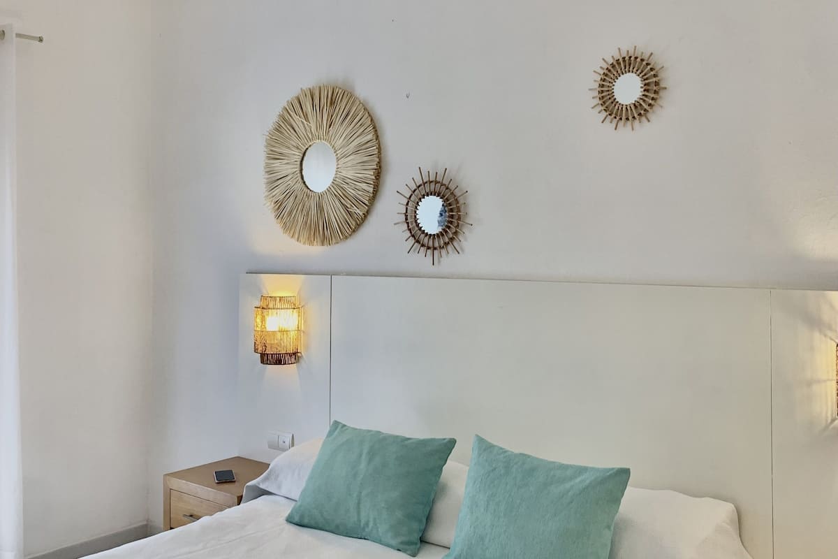 Een slaapkamer met een bed, twee kussens, een nachtkastje, een wandlamp en een plafondventilator.