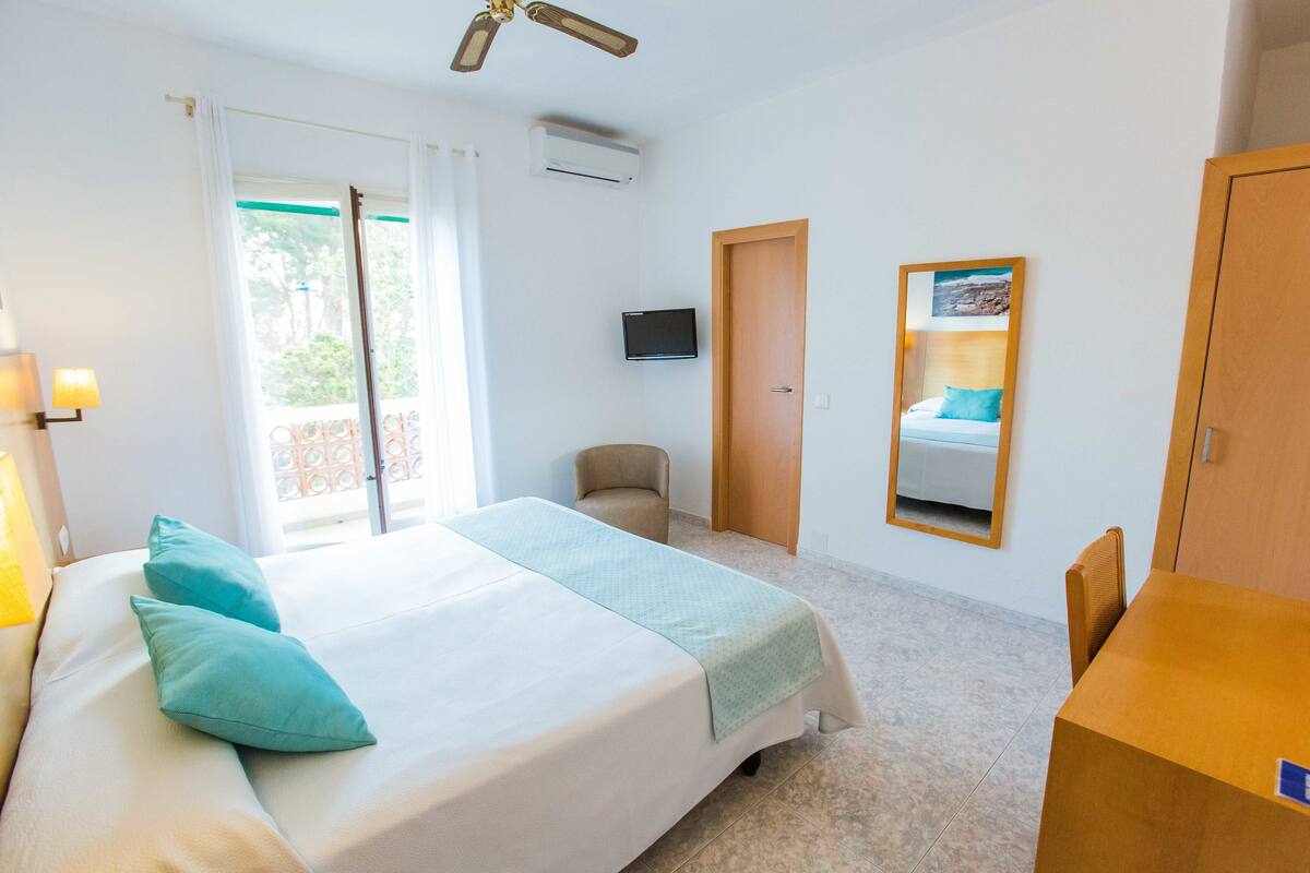 Ein Hotelzimmer mit einem Bett, einem Sessel, einem Schreibtisch, einem Fernseher und einer Tür.