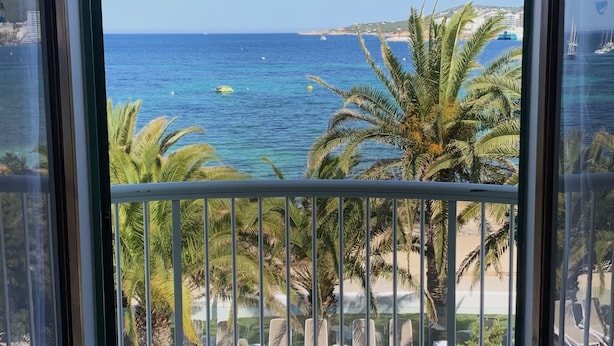 Un balcon avec vue sur la mer, des palmiers et des chaises longues.