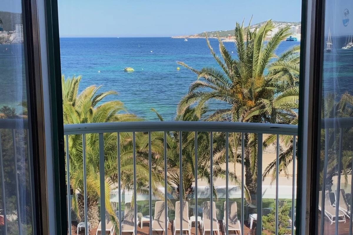 Een balkon met uitzicht op zee, palmbomen en ligstoelen.
