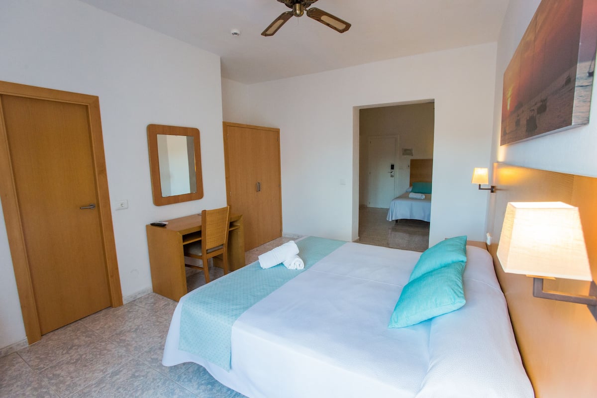 Een hotelkamer met een bed, een bureau, een stoel, een spiegel en een plafondventilator.