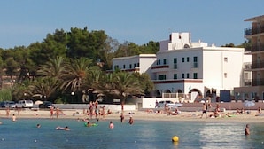 Une plage où l’on voit des gens nager et bronzer, des palmiers et un bâtiment blanc doté de balcons.