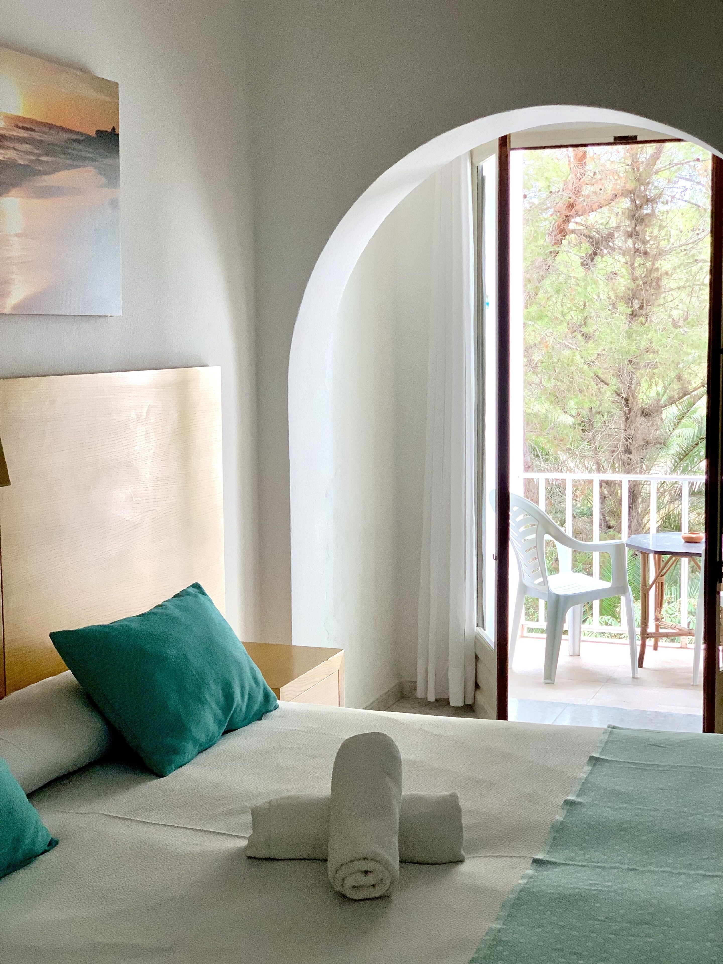 Habitación de hotel con cama, vistas al exterior y un balcón con mesa y sillas.