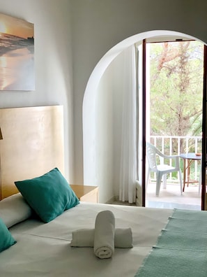 Habitación de hotel con cama, vistas al exterior y un balcón con mesa y sillas.