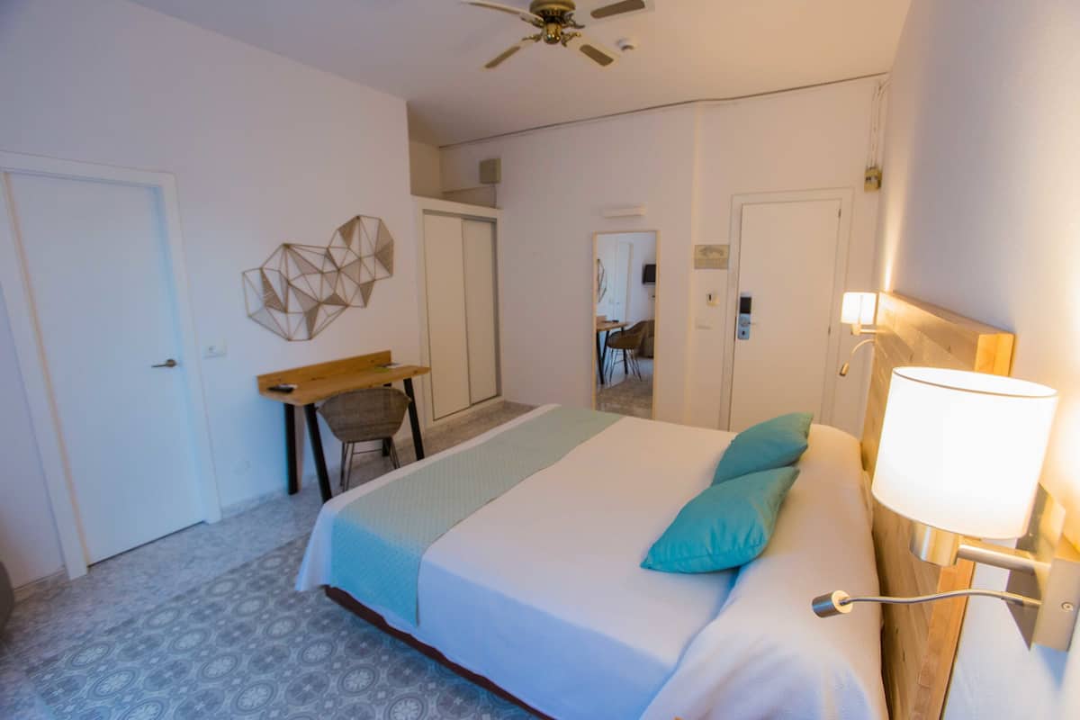 Een hotelkamer met een bed, bureau, stoel en plafondventilator.