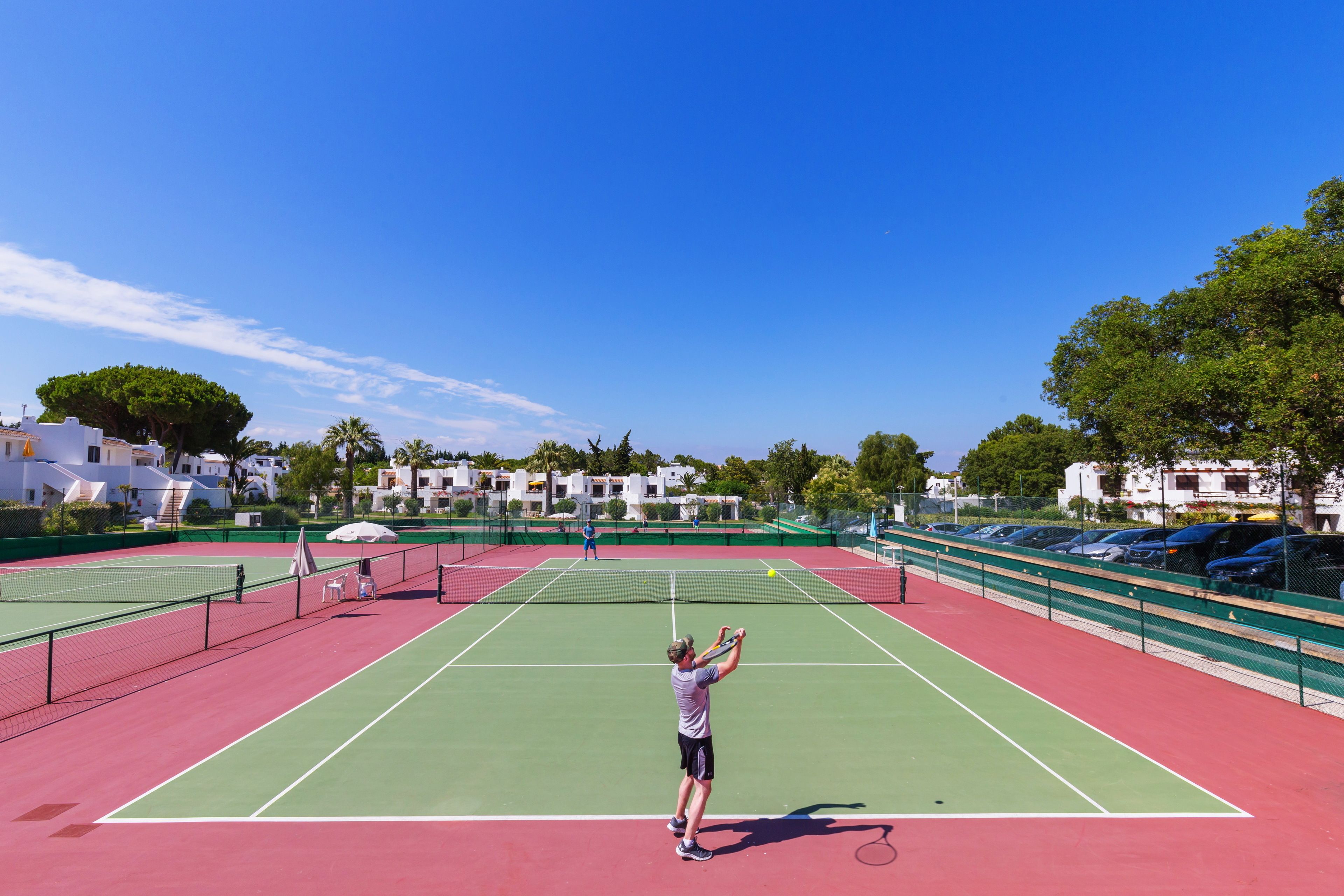 En tennisbane med net, grønne og røde spilleområder, og en person der spiller tennis.