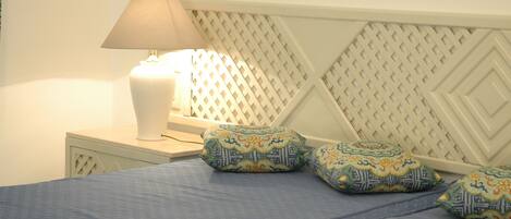 A neatly made bed with a blue bedspread and decorative pillows, a bedside lamp, and a patterned headboard.