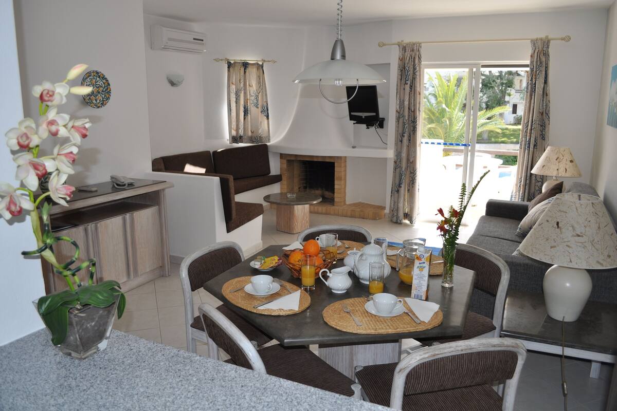A dining area with a table set for breakfast, a sofa, and a fireplace.