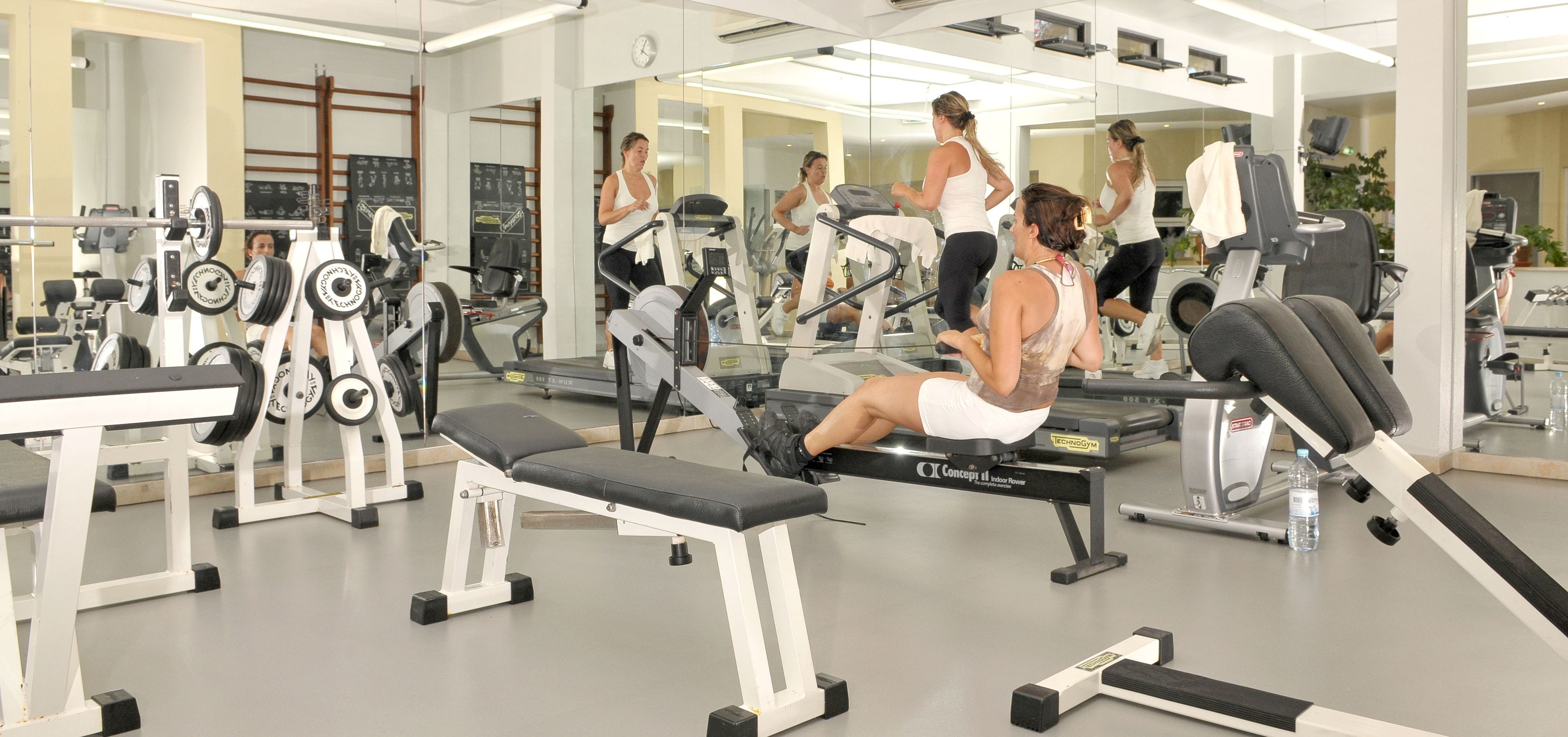 Uma academia com diversos equipamentos de exercício, incluindo esteiras, aparelhos de musculação e bancos.