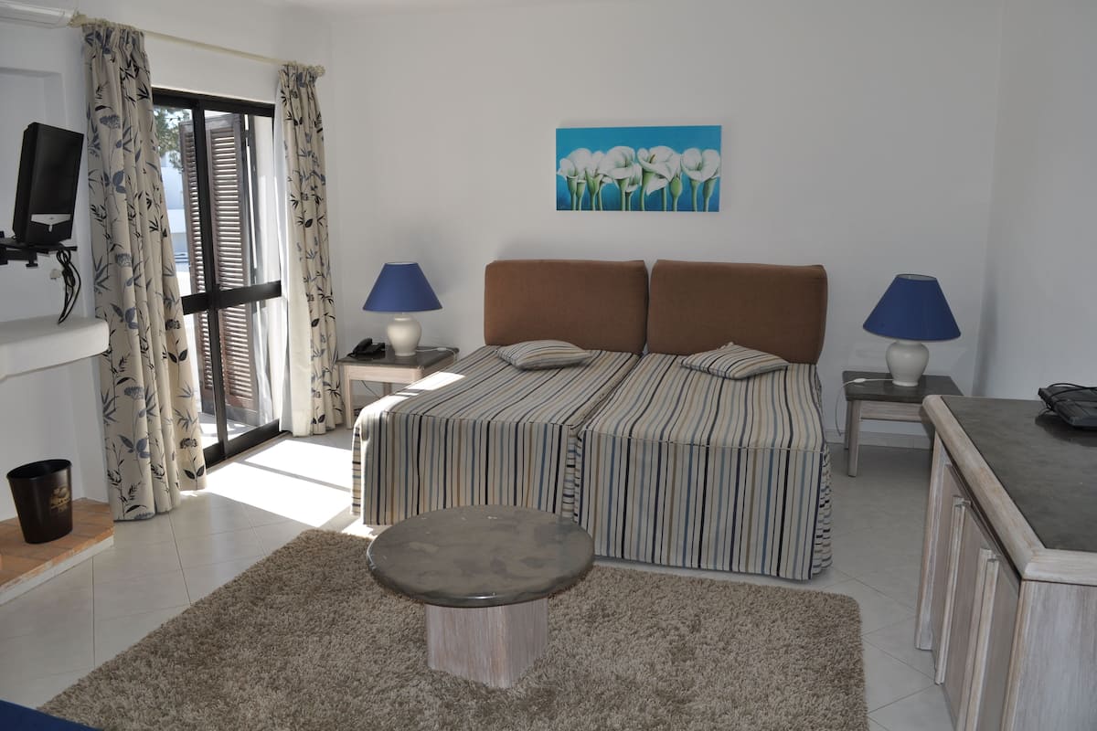 A bedroom with a bed, two bedside tables with lamps, a TV, a painting, and a sliding glass door.