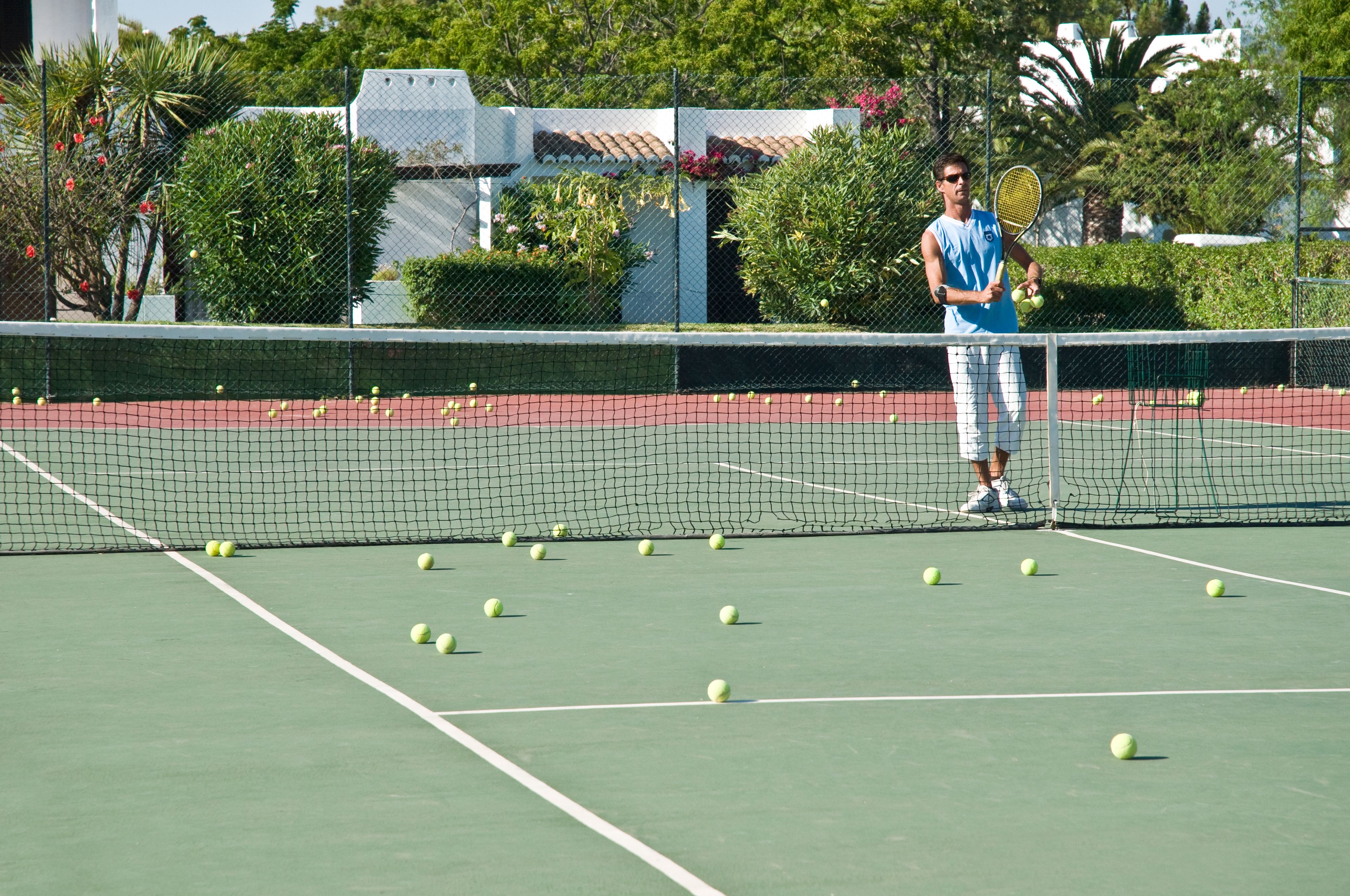 Un court de tennis avec un filet au milieu, entouré de verdure et avec un bâtiment en arrière-plan.