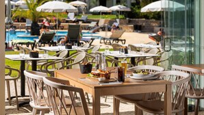 An outdoor dining area with tables and chairs, a pool in the background, and umbrellas. - Balaia Golf Village Resort (Albufeira)