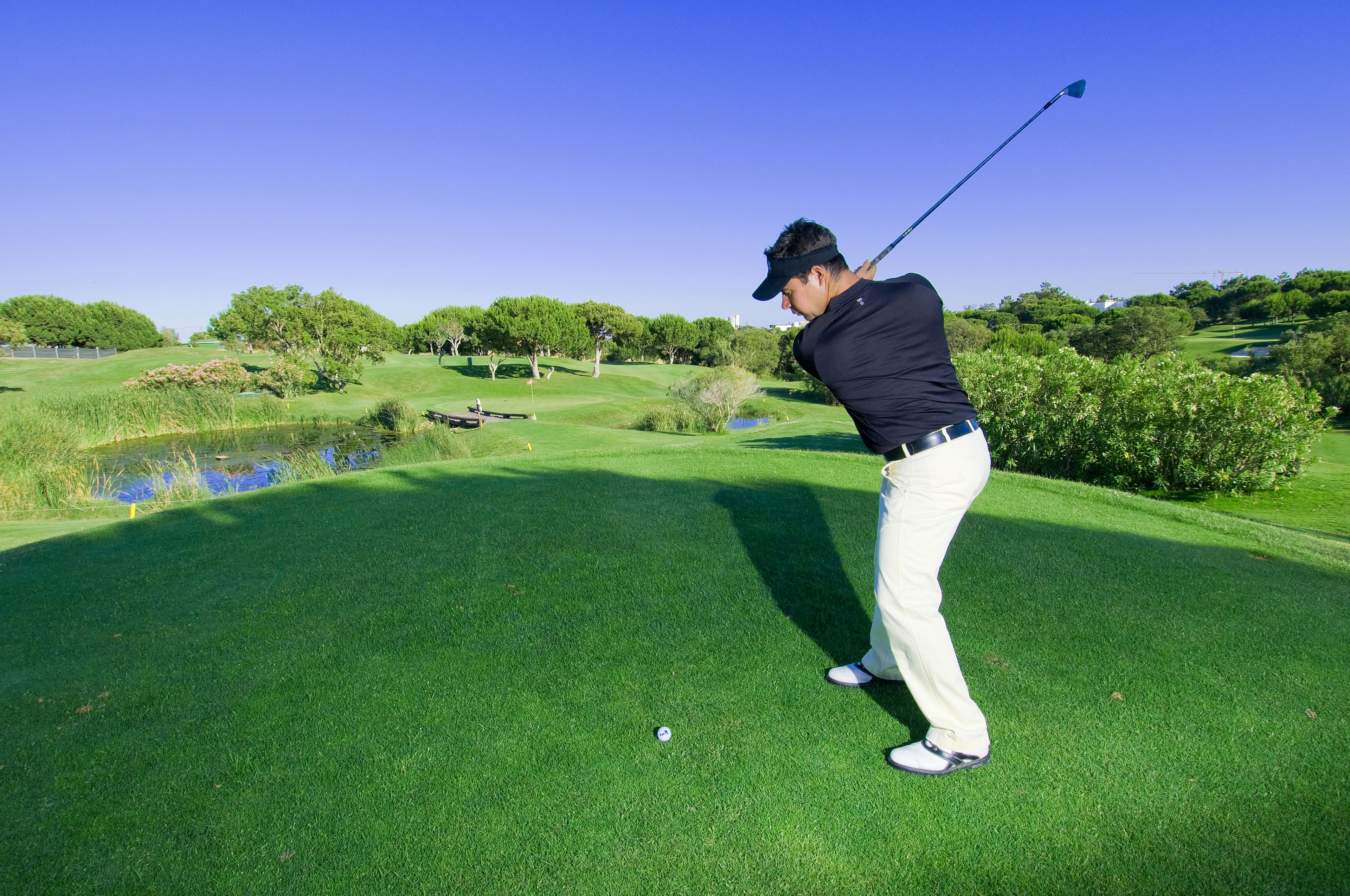 Un campo de golf con cielo despejado, césped cuidado y un cuerpo de agua.
