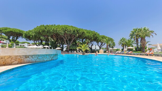 A swimming pool with clear blue water, surrounded by lounge chairs and palm trees. - Balaia Golf Village Resort (Albufeira)