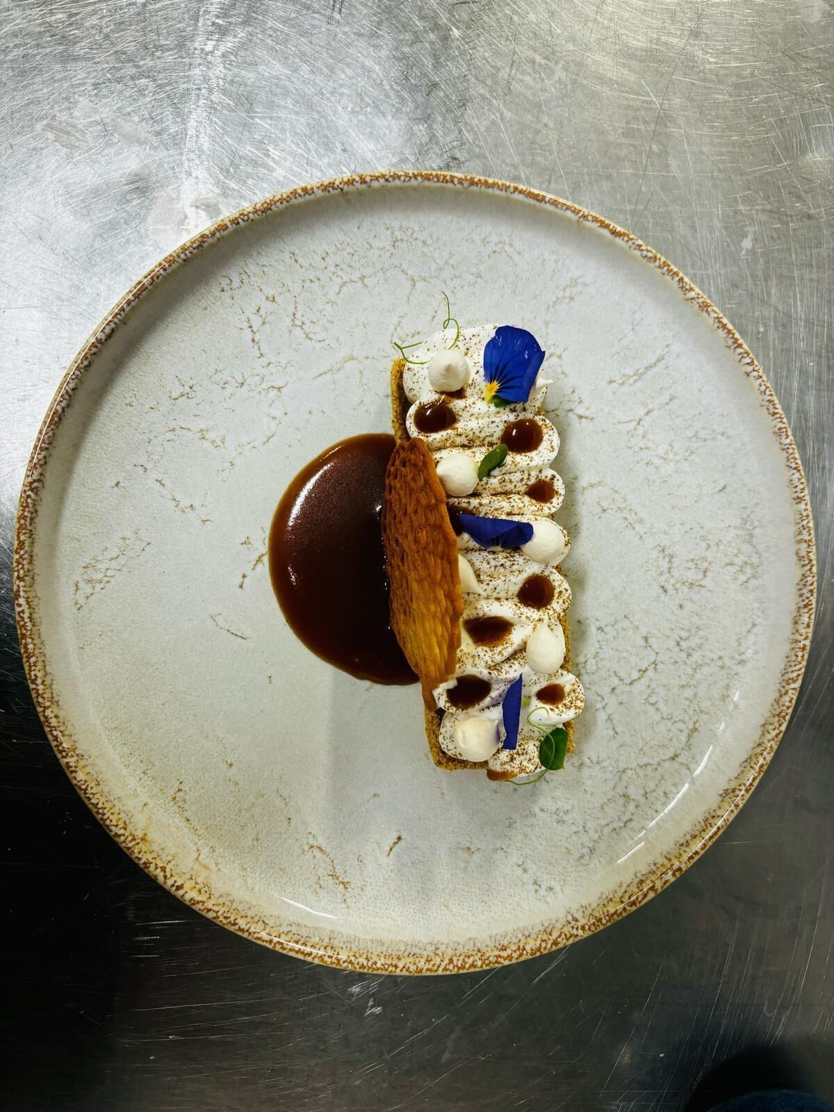 Un postre sobre un plato de cerámica con salsa de chocolate y detalles decorativos.