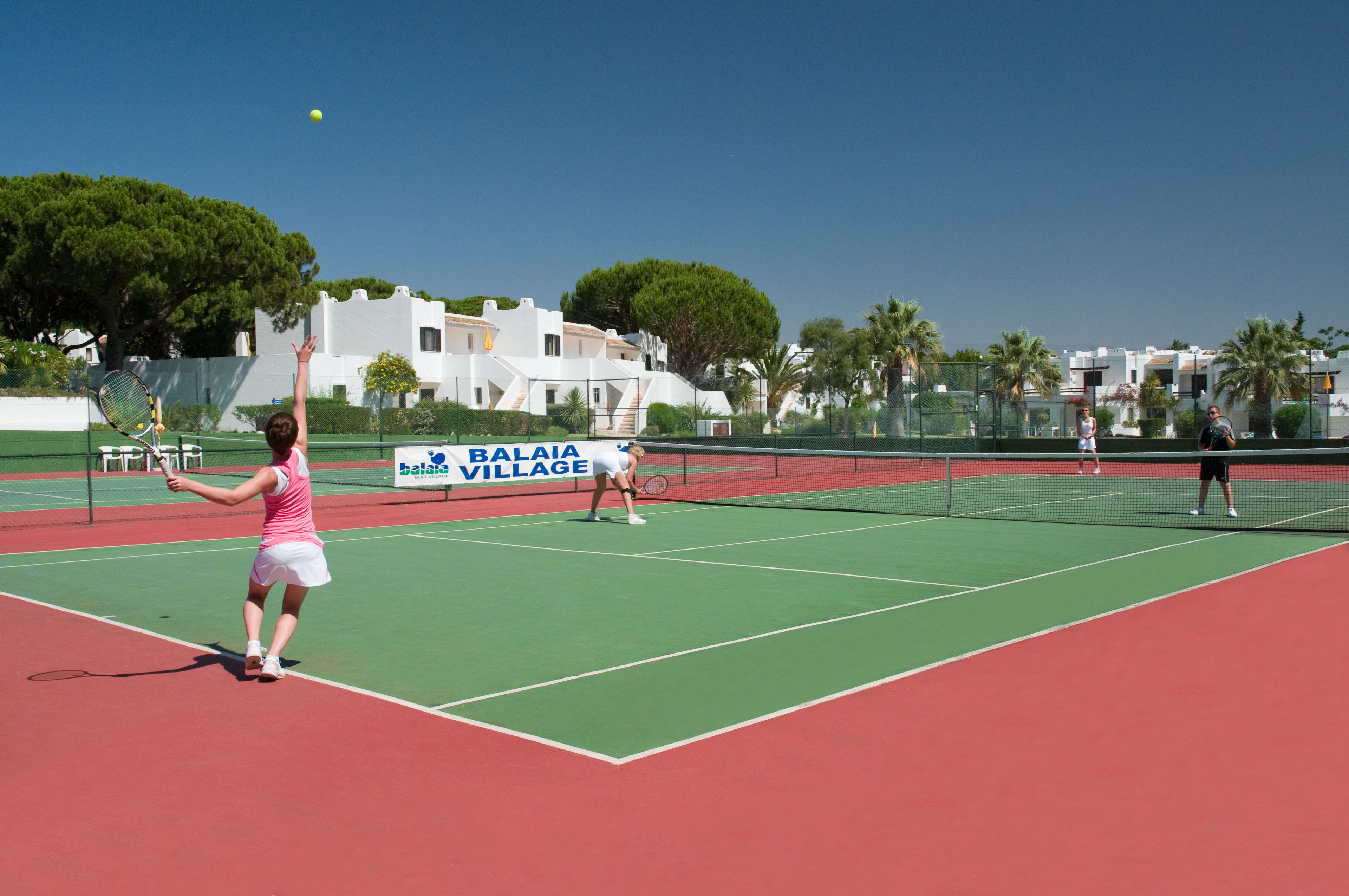 Un court de tennis avec un filet, une balle de tennis en jeu et un panneau indiquant « BALAIAVILLAGE ».