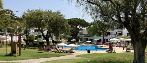 A sunny outdoor area with a swimming pool, lounge chairs, and a playground.