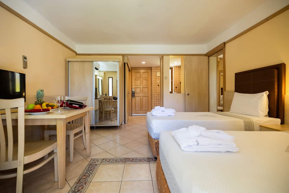 A hotel room with two beds, a dining area with a table and chairs, and a TV.