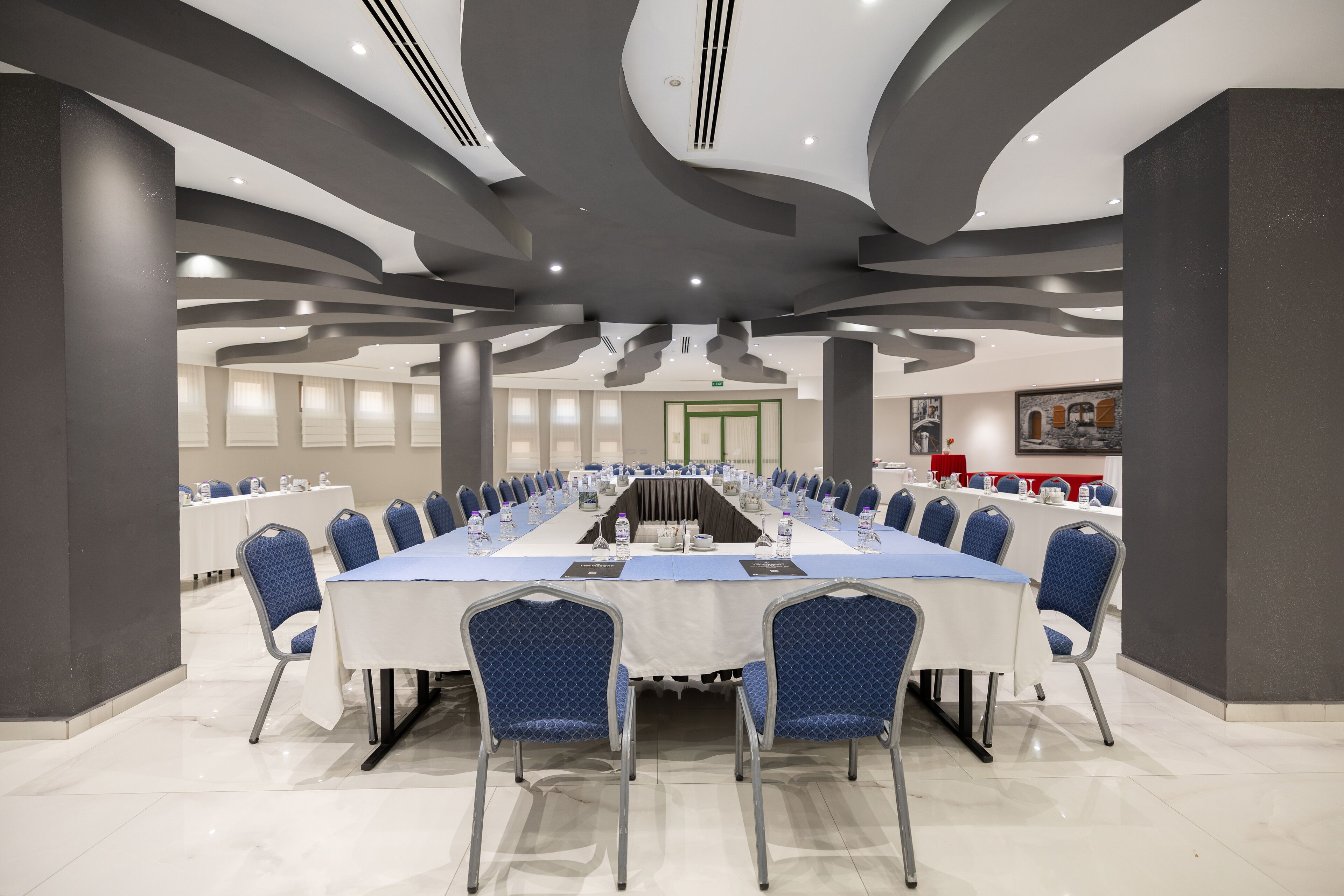 Un salón de conferencias con una larga mesa, sillas azules y un diseño de techo moderno.