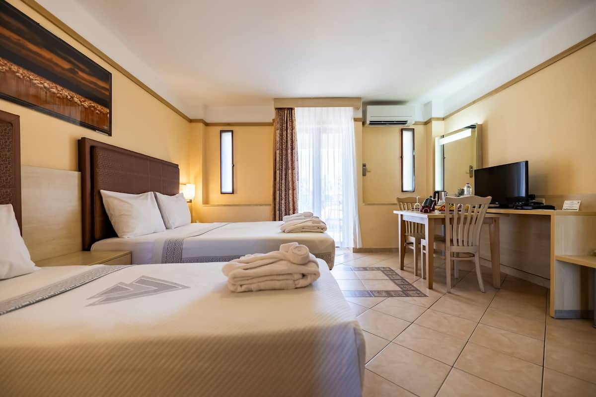 A hotel room with two beds, a desk, a chair, a television, and a large window with curtains.