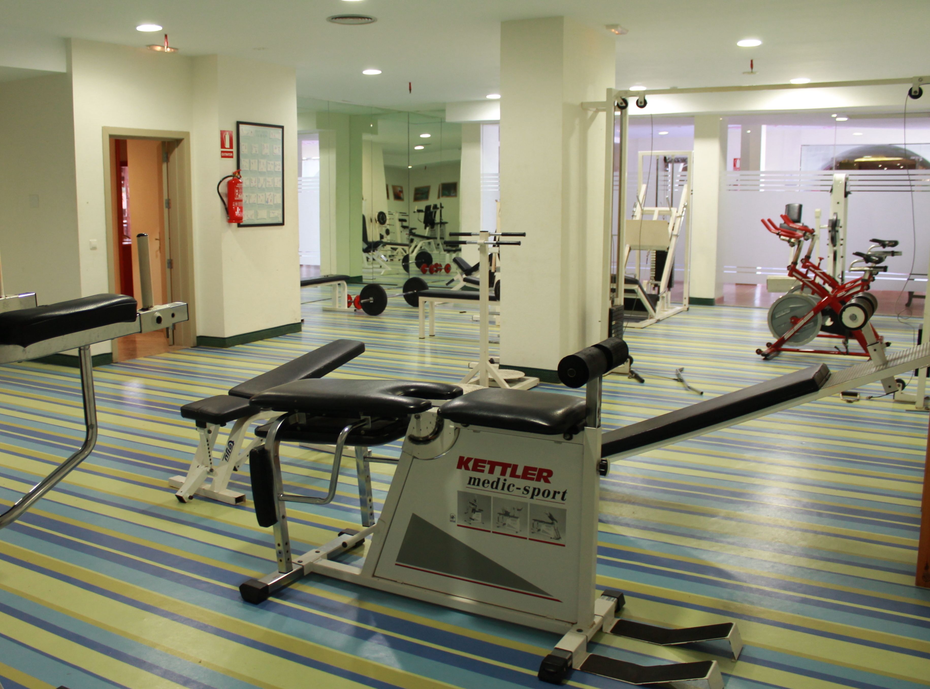 A gym with exercise equipment, a bench, and a mirrored wall.