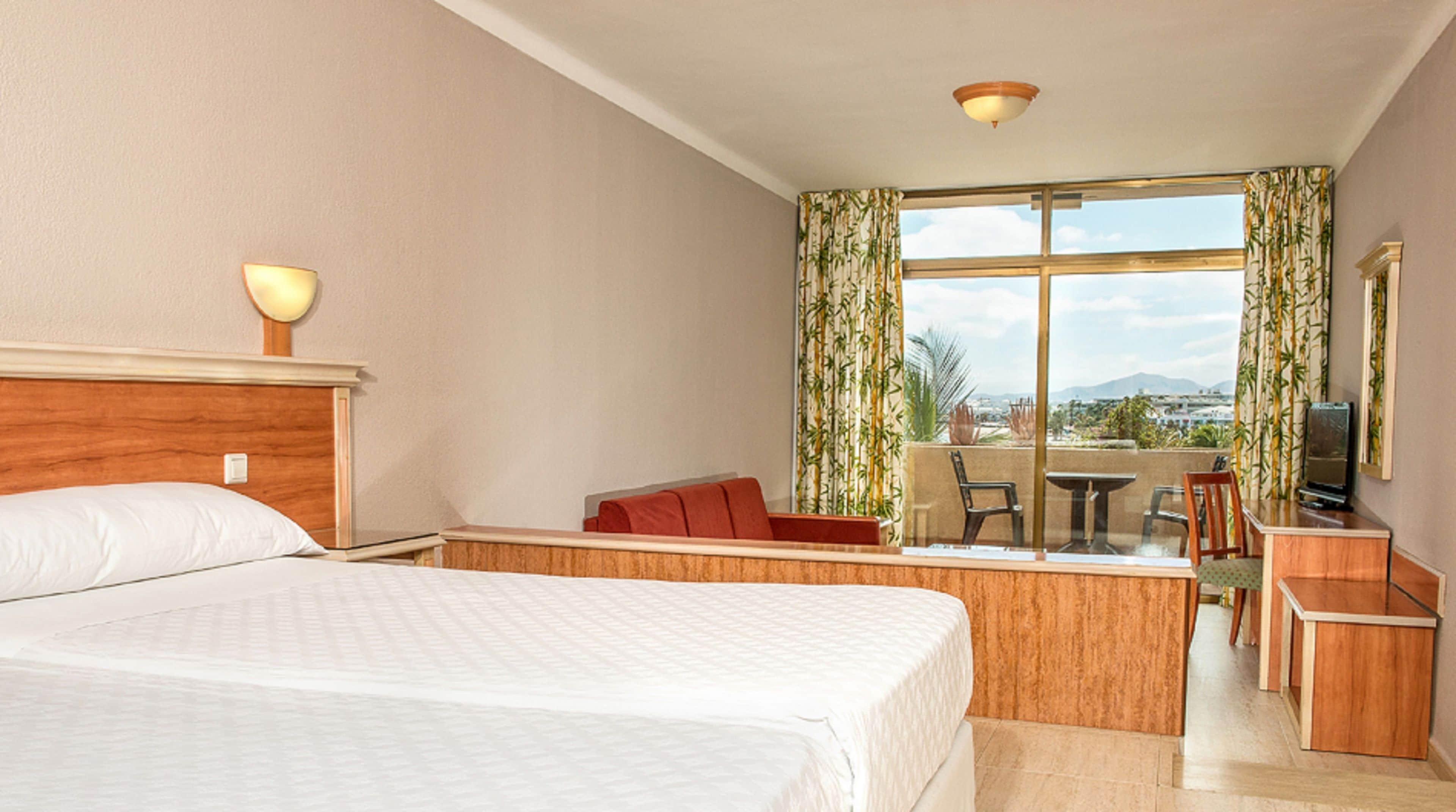 A hotel room with a bed, a desk, a chair, a TV, and a window with curtains.