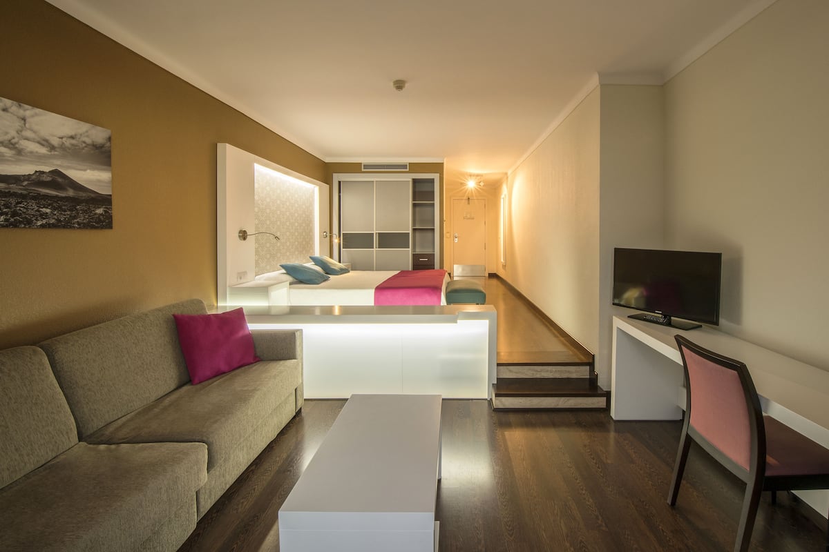 A modern living room with a sofa, a coffee table, a TV, and a staircase leading to a bedroom.