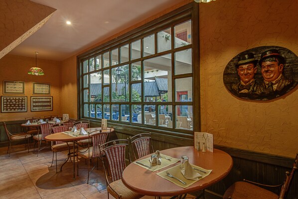 A restaurant with multiple tables and chairs, large windows, and framed pictures on the walls.