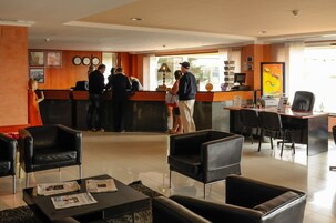 A hotel reception area with a counter, several black leather chairs, and a few people standing at the counter.