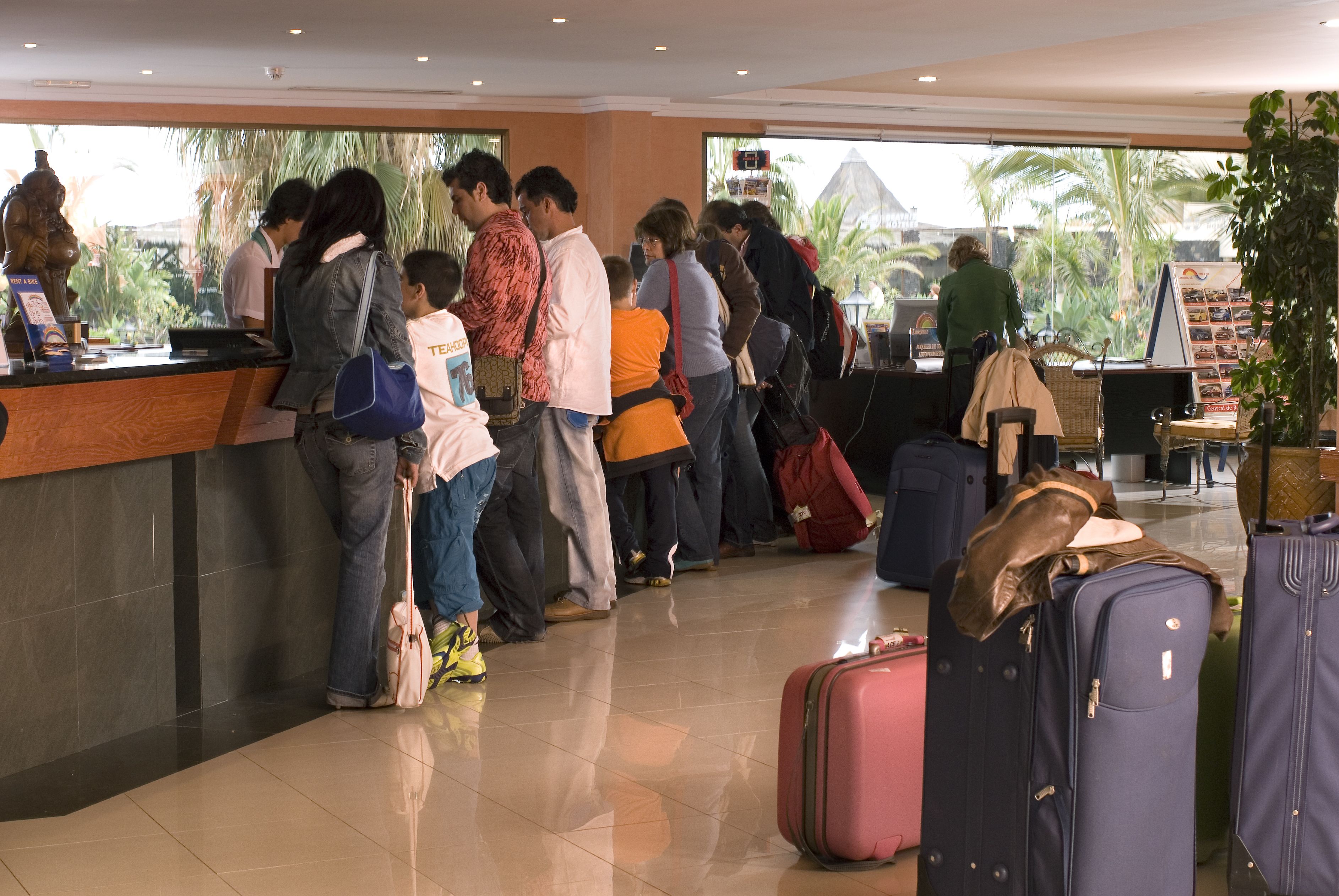 A hotel reception area with a counter, people waiting, and luggage.