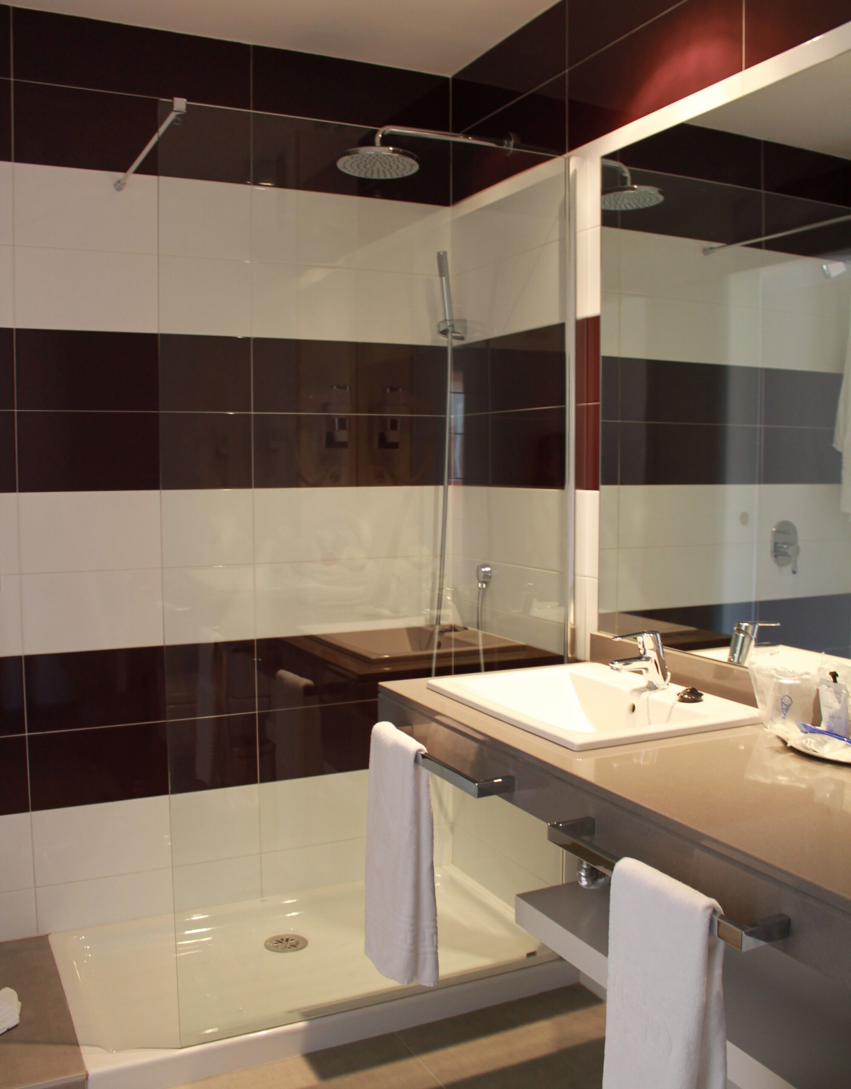 Un baño moderno con ducha envuelta en vidrio, tocador con lavamanos y espejo, y dos toallas sobre la encimera.