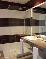 A modern bathroom with a glass-enclosed shower, a vanity with a sink and mirror, and two towels on the counter.