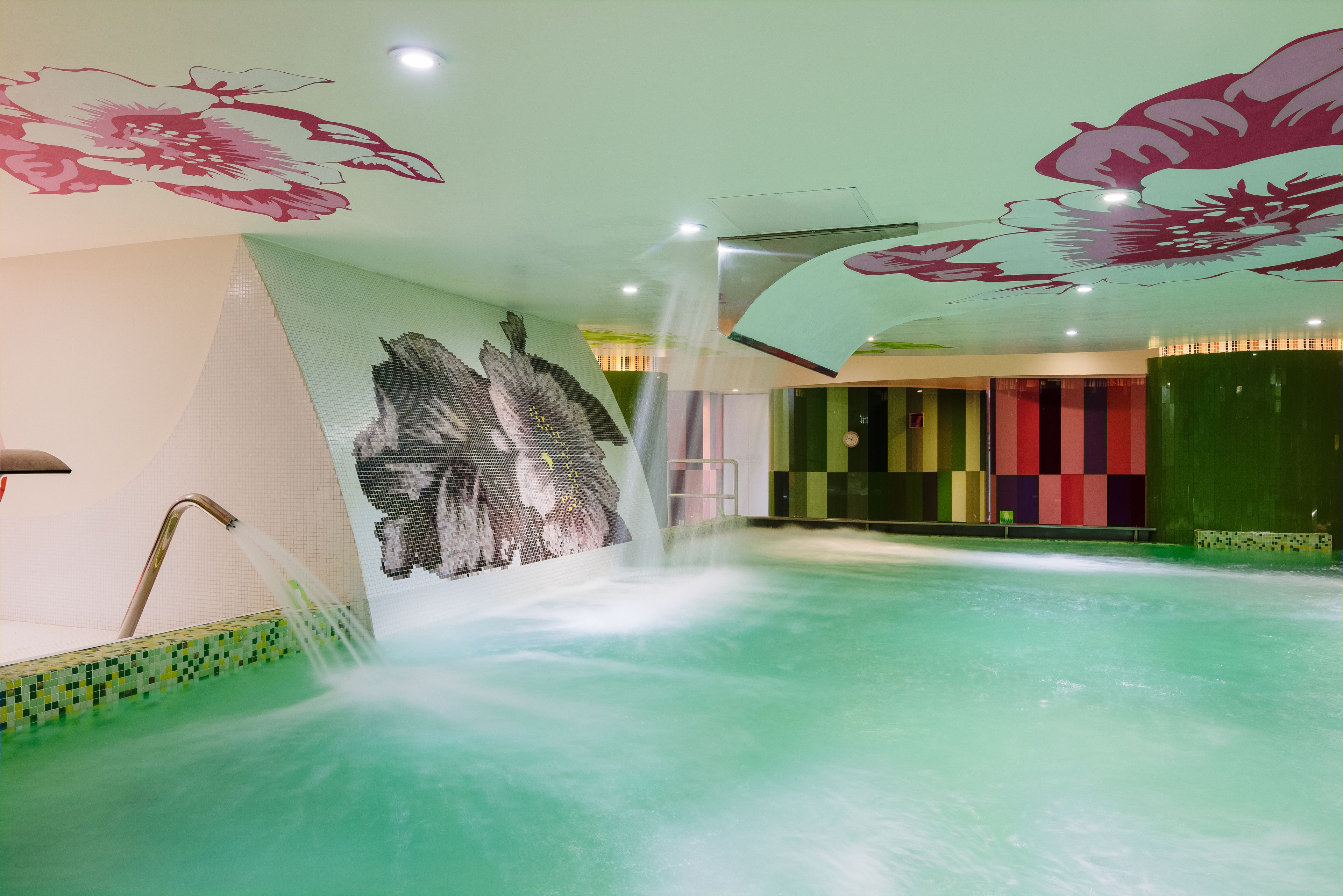 Una piscina con una fontana, un murale al muro e un design colorato.