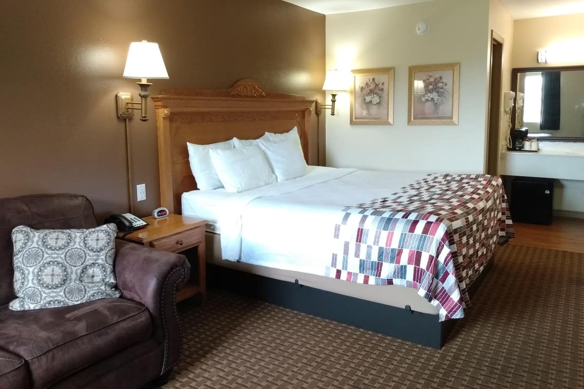 A hotel room with a large bed, a wooden headboard, a nightstand, a desk, a chair, and a mirror.