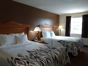 A hotel room with two beds, wooden headboards, bedside lamps, and a window with curtains.
