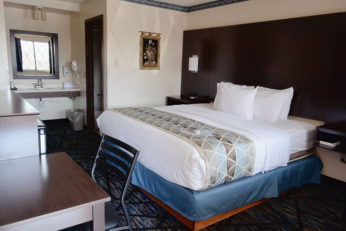 A hotel room with a bed, desk, chair, and a small table.