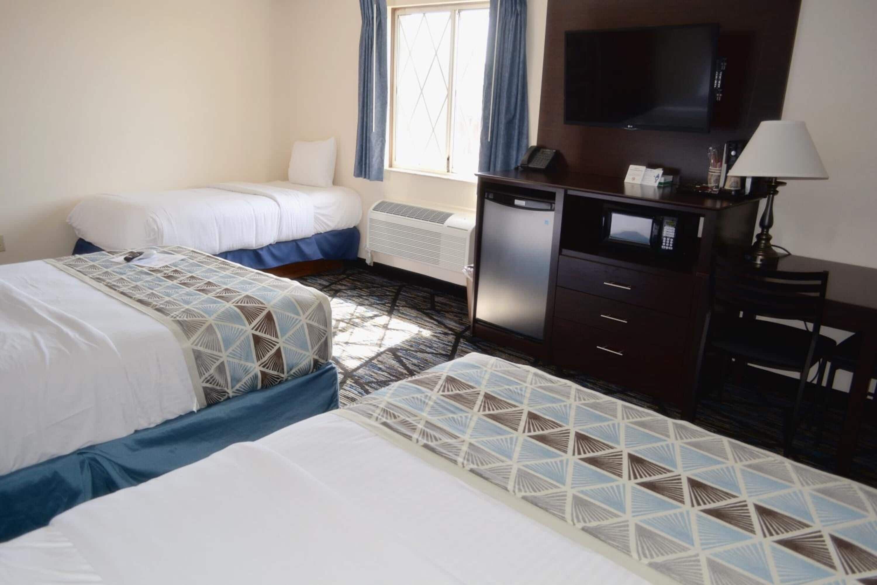 A hotel room with two beds, a desk with a lamp, a television, and a minibar.