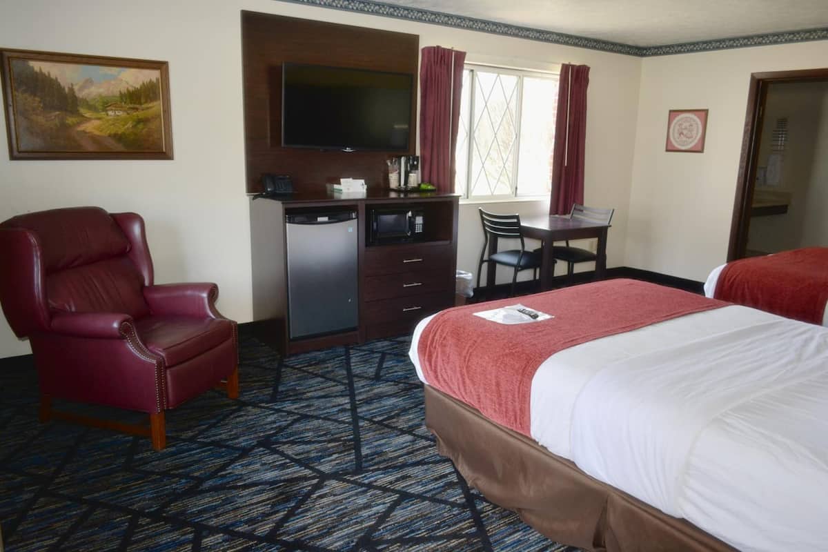 A hotel room with a bed, a desk with a chair, a television, and a red leather chair.