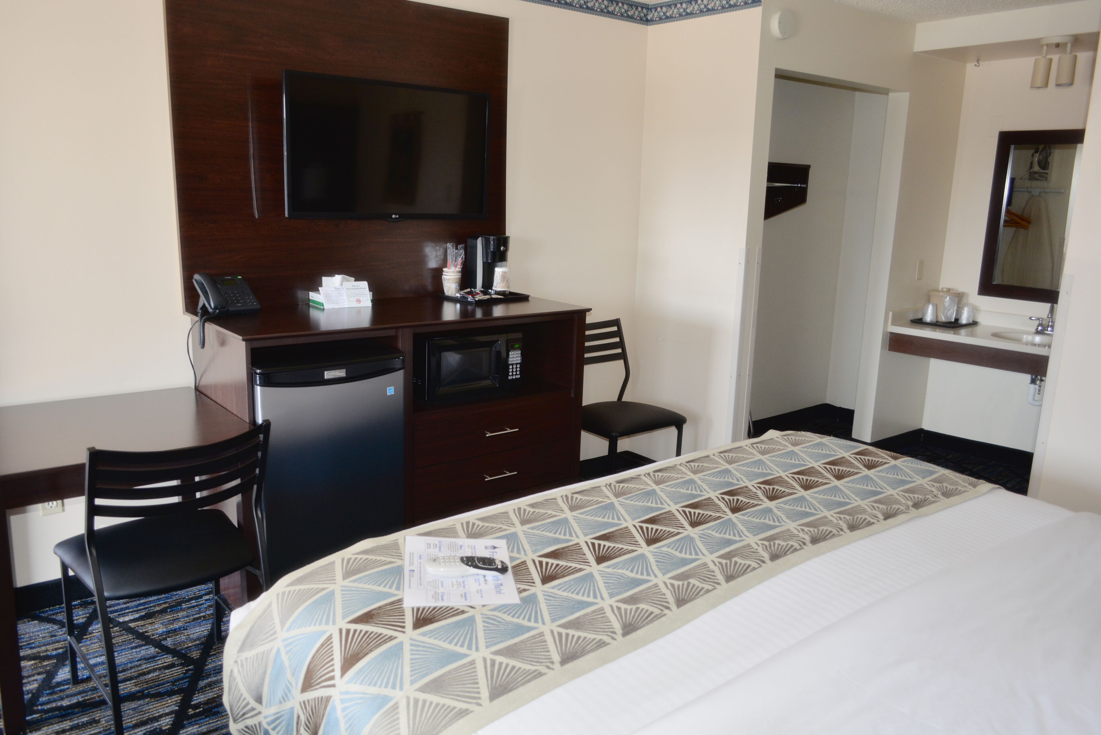 Una habitación de hotel con una cama, un escritorio con teléfono y microondas, una silla y un televisor en la pared.