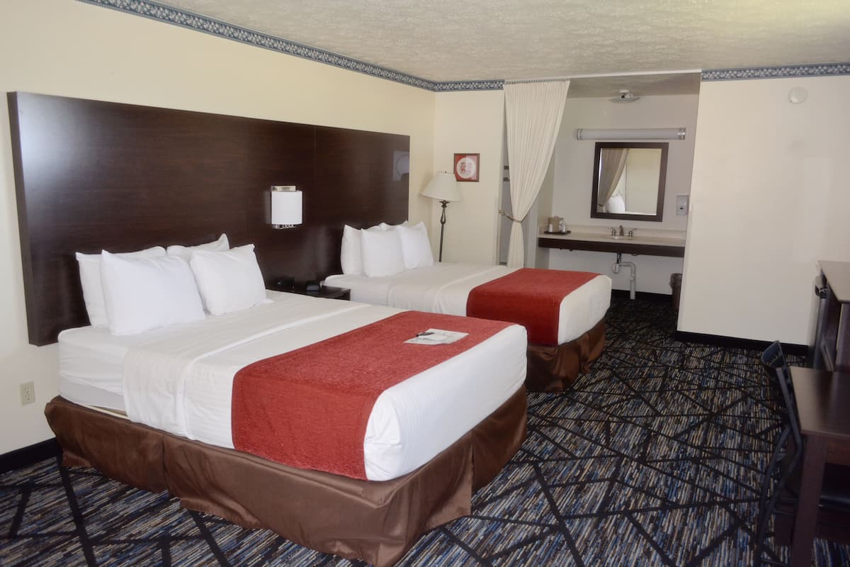 A hotel room with two beds, a bathroom, and a desk.