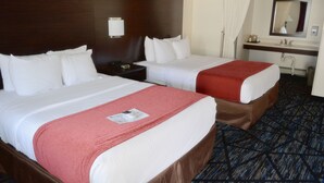 Habitación de hotel con dos camas, una mesita de noche, un espejo y un baño con lavamanos y espejo.