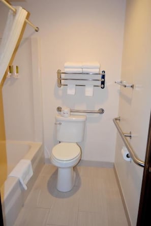 A small, clean bathroom with a toilet, a handrail, and a towel rack. - Frankenmuth Motel (Frankenmuth)