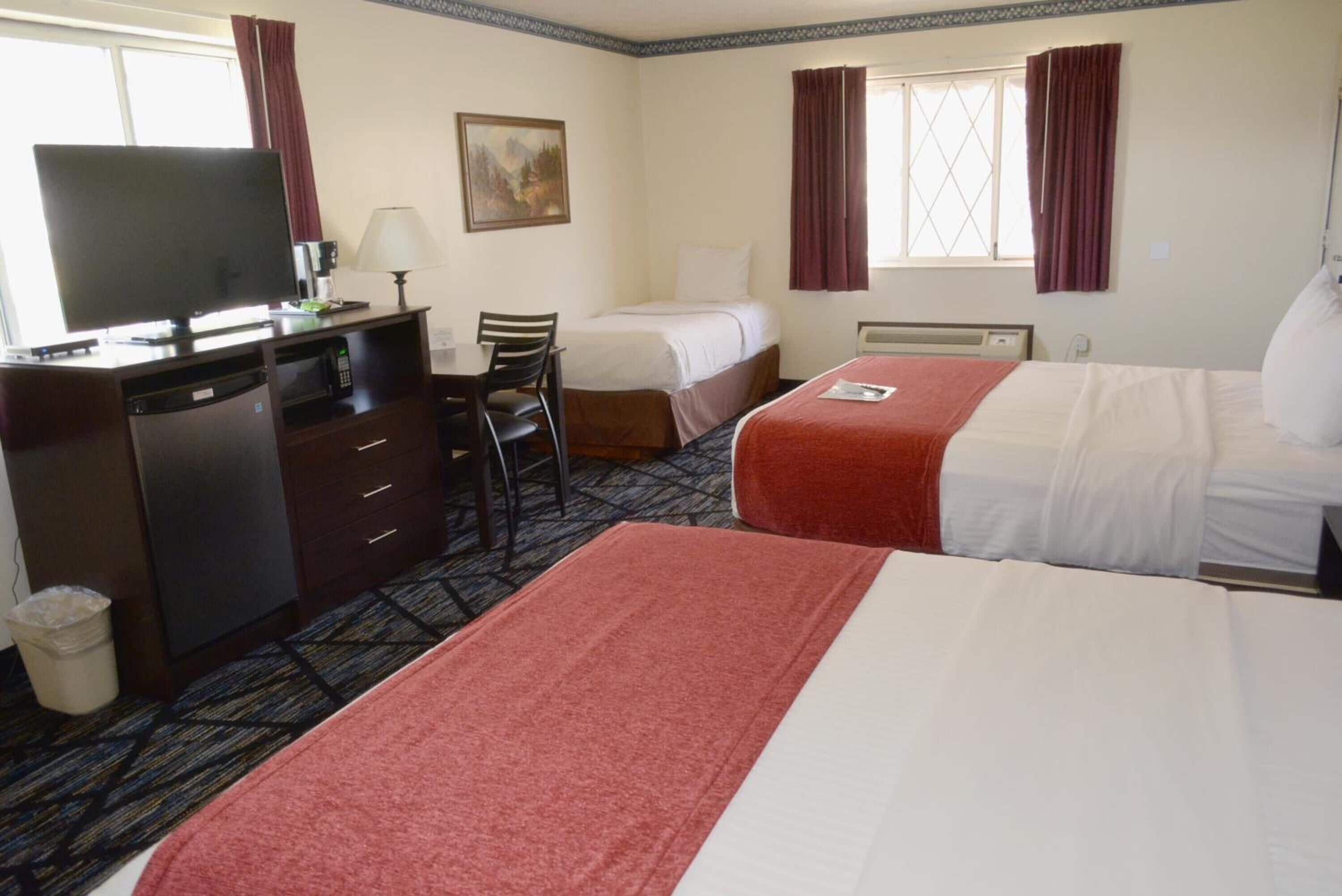 A hotel room with two beds, a desk with a television, a chair, and a waste bin.