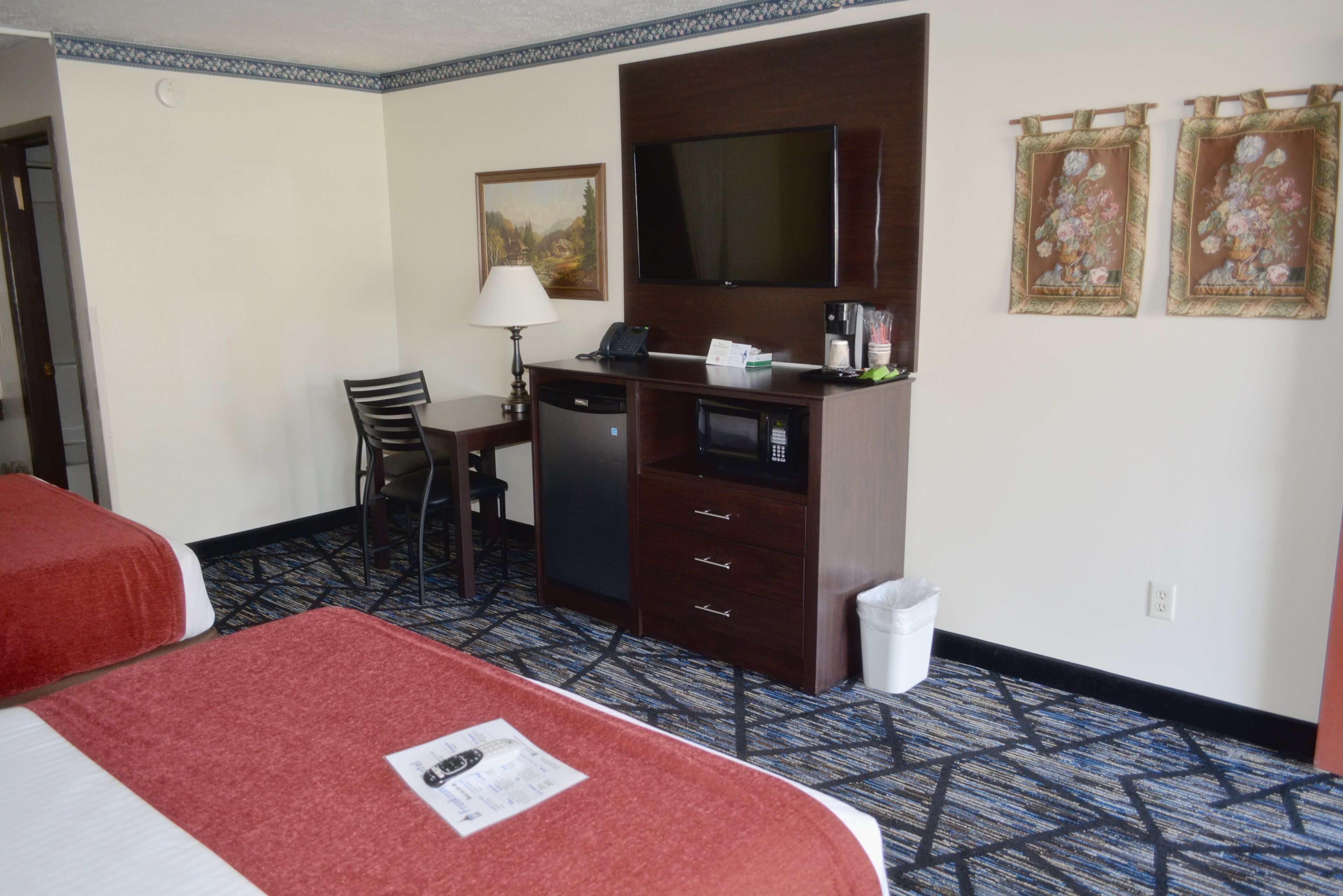 A hotel room with two beds, a desk with a telephone, a microwave, and a television.